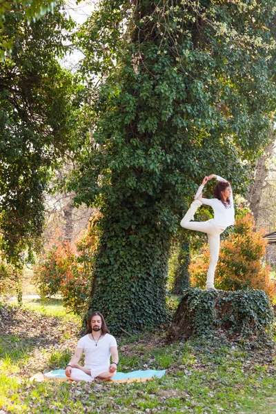 Joven hombre y mujer practican yoga al aire libre en madera día de verano — Foto de Stock
