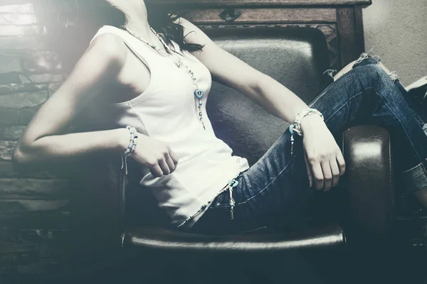 woman indoor sit in armchair wearing blue jeans and white tank s