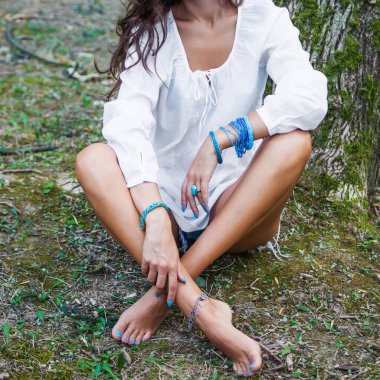 Çıplak ayaklı, bembeyaz keten gömlekli bir kadın vücudu çimenlere oturur. Bir sürü turkuaz boncuk bilezik, yüzük ve bileklik takar.