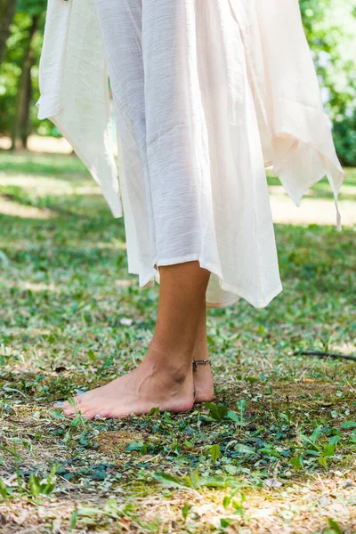 光着脚的女人穿着长长的亚麻布衣服站在公园的草地上 — 图库照片
