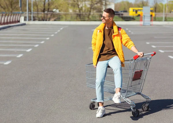 スーパー マーケット駐車場で食物からカートに座っているサングラスと黄色のジャケットのファッション男 — ストック写真