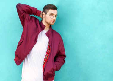 Gözlüklü moda hipster adam duvara yakın ekşi dalga rengini pozlar.
