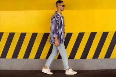 çizgili bir gömlek moda adam sarı Park duvara yakın duruyor