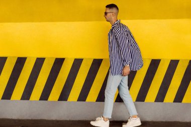 çizgili bir gömlek moda adam sarı Park duvara yakın duruyor