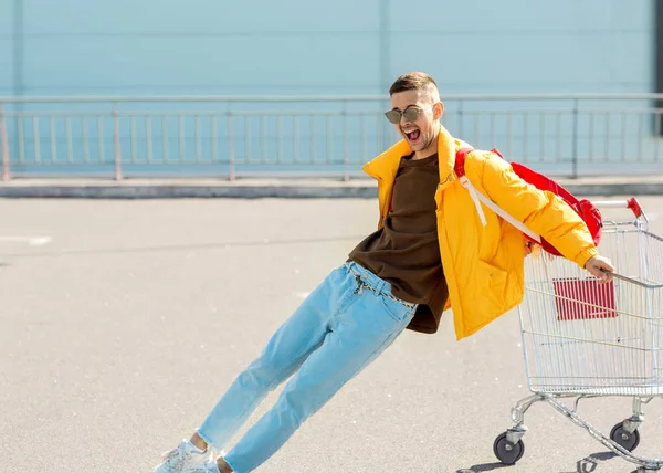 Парень Солнцезащитных Очках Желтая Куртка Прыгают Тележку Еды Парковке Супермаркета — стоковое фото