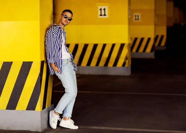 fashion guy in a striped shirt is standing near a yellow parking wall