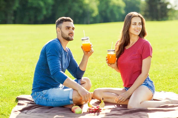couple in love have fun in the park and drink smoothies and eating fruit at a picnic