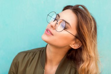 Turkuaz bir duvara yakın poz yuvarlak gözlük standları kız moda