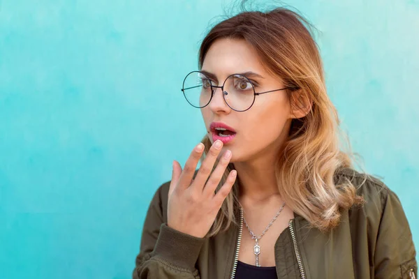 fashion girl in round glasses stands posing near a turquoise wall