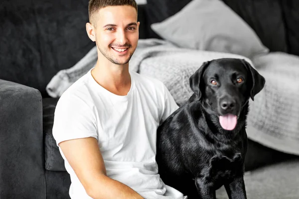 家で座っているフリーランサー男を抱擁で犬と一緒に働いて黒のラブラドール — ストック写真