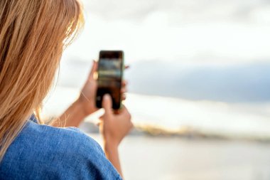 kız bir manzara, gün batımında onun elinde bir telefon yakın çekim fotoğraf çekmek