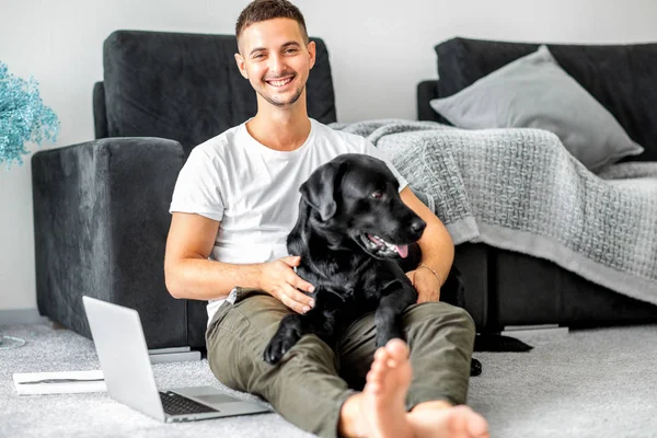 家で座っているフリーランサー男を抱擁で犬と一緒に働いて黒のラブラドール — ストック写真