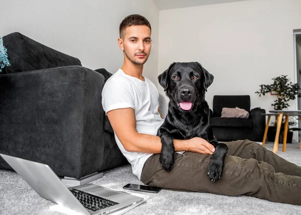 家で座っているフリーランサー男を抱擁で犬と一緒に働いて黒のラブラドール — ストック写真
