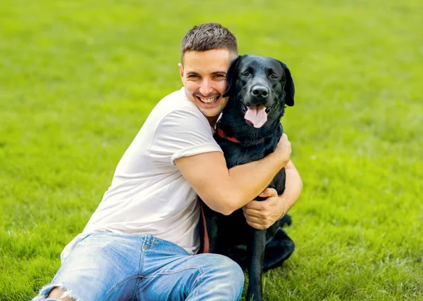 男が公園で遊んで彼の犬のラブラドールとハグ — ストック写真