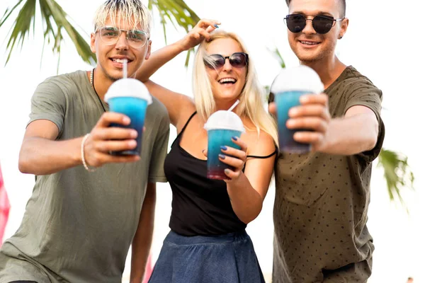 three friends cheerful company rest on a tropical beach and drink cocktails, very, magazine concept