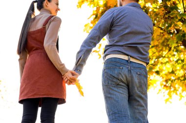 Birbirine aşık genç bir çift sonbahar parkında el ele tutuşup gün batımına bakıyor.