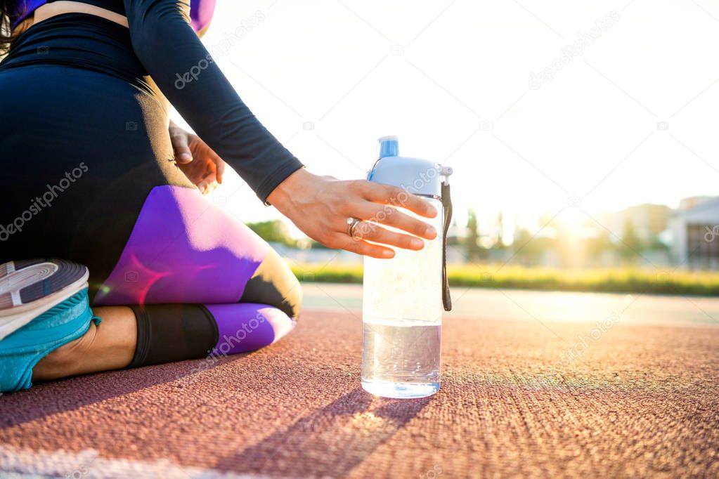 girl sportsman crossfit and squats agains and drinks water at sunset