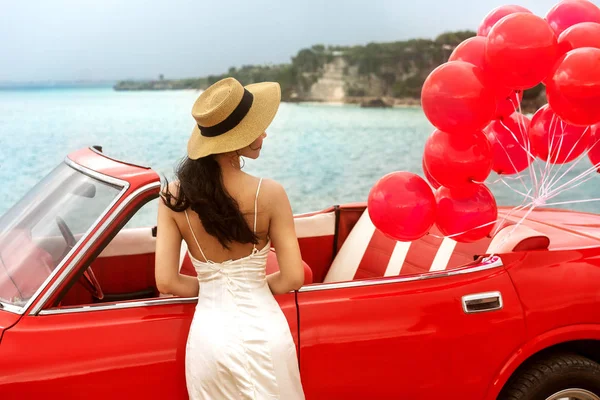 Girl at the wedding in a white dress stands near the red retro car — Stock Photo, Image