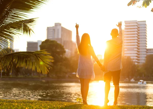 Couple in love at sunset stands back in tropical palms with a view to the metropolis, rear view — Stock Photo, Image