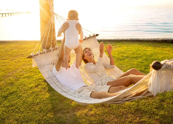 Glückliche Familie auf einer tropischen Insel bei Sonnenuntergang in einer Hängematte liegen und mit ihrem Sohn spielen — Stockfoto