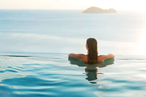 Chica en la piscina al atardecer con vistas a las montañas y al mar — Foto de Stock