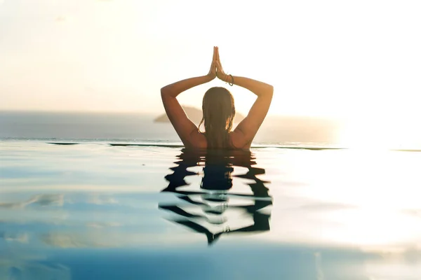 Chica en la piscina al atardecer haciendo yoga con vistas al mountai —  Fotos de Stock