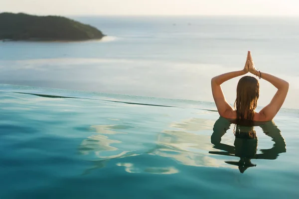 Ragazza in piscina al tramonto facendo yoga con vista sulle montagne e sul mare — Foto Stock