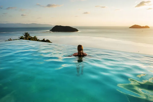 Ragazza in piscina al tramonto con vista sulle montagne e sul mare — Foto Stock