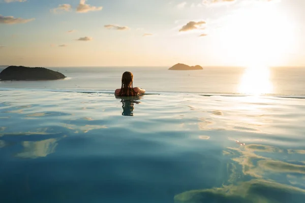 Ragazza in piscina al tramonto con vista sulle montagne e sul mare — Foto Stock