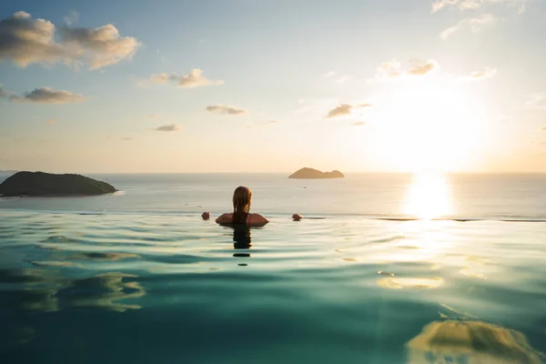 Mädchen im Pool bei Sonnenuntergang mit Blick auf die Berge und das Meer — Stockfoto