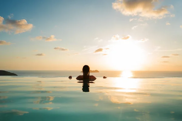 Ragazza in piscina al tramonto con vista sulle montagne e sul mare — Foto Stock