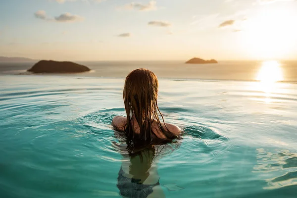 Ragazza in piscina al tramonto con vista sulle montagne e sul mare — Foto Stock