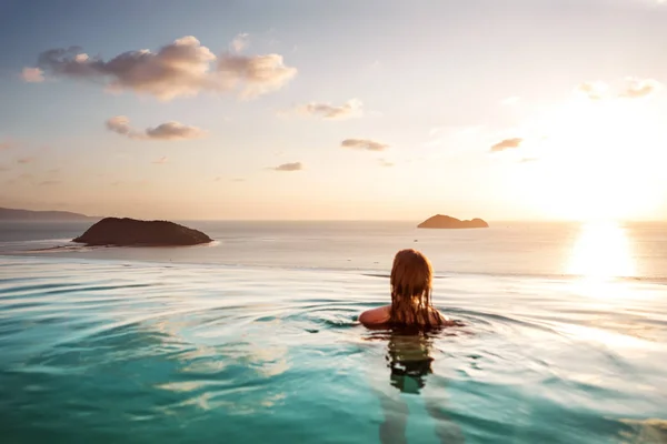 Ragazza in piscina al tramonto con vista sulle montagne e sul mare — Foto Stock