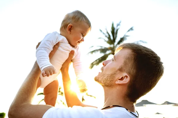 Vader en zoon spelen op het strand in tropische palmbomen bij zonsondergang, vaderdag. — Stockfoto