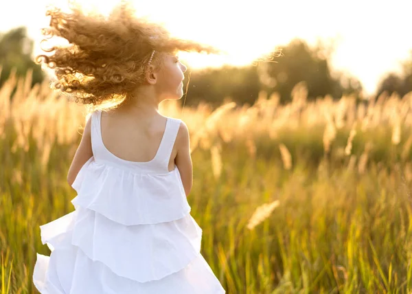 Mała dziewczynka w zachodzie słońca odgrywa w polu — Zdjęcie stockowe