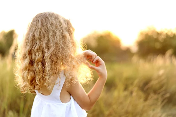 Little girl at sunset shows a heart with hands plays in the field — Stock Photo, Image