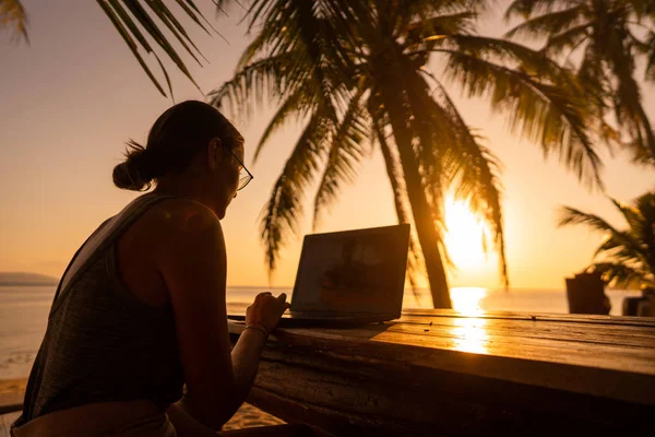 Freelance fille avec un ordinateur parmi les palmiers tropicaux travailler sur l'île au coucher du soleil — Photo