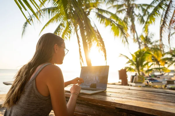 Фрілансер дівчина з комп'ютером серед тропічних пальм працює на острові під час заходу сонця — стокове фото
