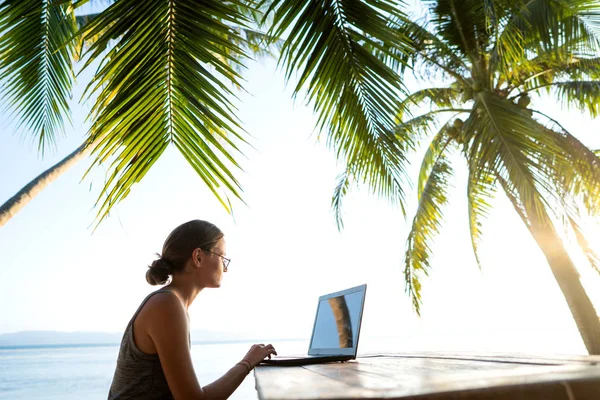 Фрілансер дівчина з комп'ютером серед тропічних пальм працює на острові під час заходу сонця — стокове фото