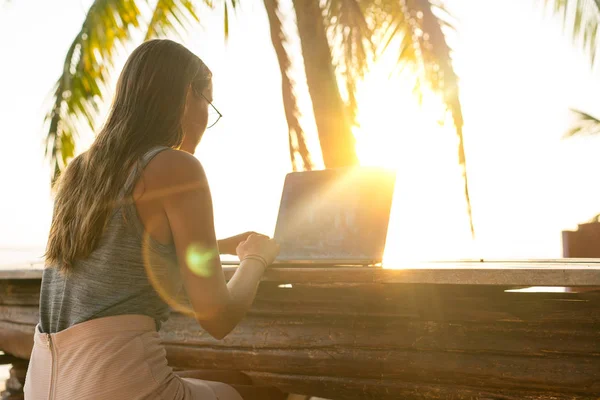 Freelancer meisje met een computer tussen tropische palmbomen werken op het eiland in zonsondergang — Stockfoto