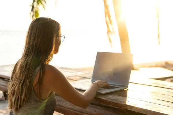 Freelance fille avec un ordinateur parmi les palmiers tropicaux travailler sur l'île au coucher du soleil — Photo