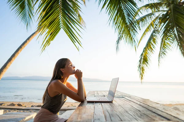 Freelance fille avec un ordinateur parmi les palmiers tropicaux travailler sur l'île au coucher du soleil — Photo