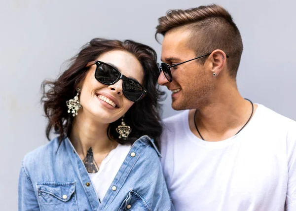 Пара моди в сонцезахисних окулярах позує на сірій стіні — стокове фото