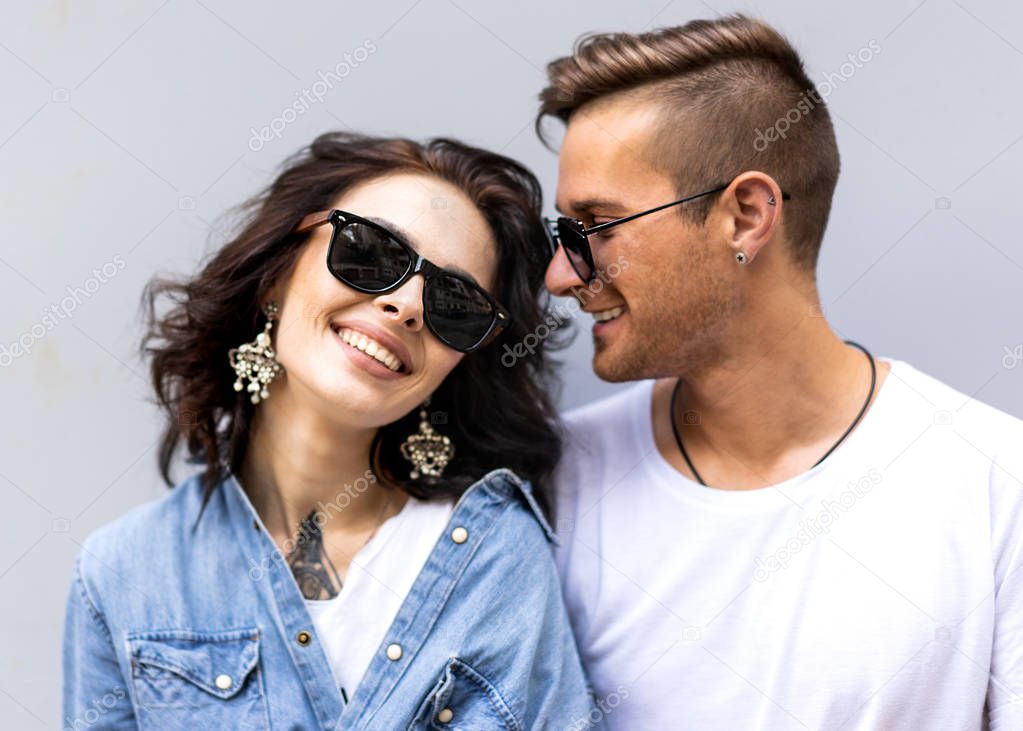 fashion couple in sunglasses posing on gray wall