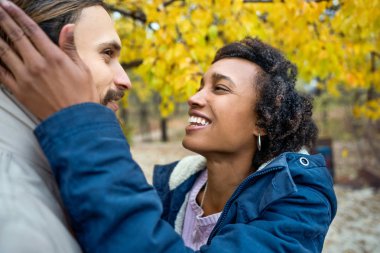 Sonbahar parkında aşık Afrikalı Amerikalı bir kızla gün batımında yürüyüşe çıkan bir adam.