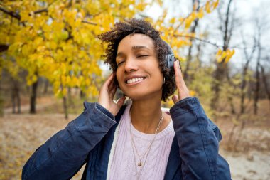 Sonbahar parkında güzel bir Afrikalı kız açık havada gülerek müzik dinliyor.