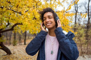 Sonbahar parkında güzel bir Afrikalı kız açık havada gülerek müzik dinliyor.