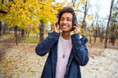Sonbahar parkında güzel bir Afrikalı kız açık havada gülerek müzik dinliyor.