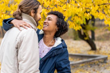 Sonbahar parkında aşık Afrikalı Amerikalı bir kızla gün batımında yürüyüşe çıkan bir adam.
