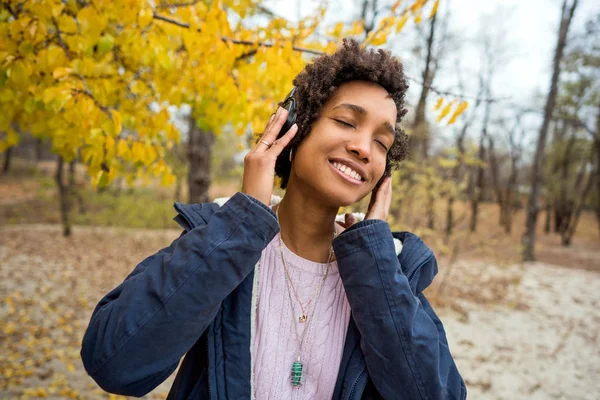 Hermosa chica africana en el parque de otoño escuchando música al aire libre sonriendo — Foto de Stock